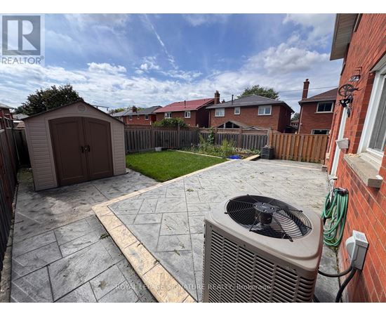 A backyard with a patio, a shed, and a wall-mounted air conditioning unit.