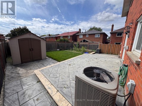 A backyard with a patio, a shed, and a wall-mounted air conditioning unit.