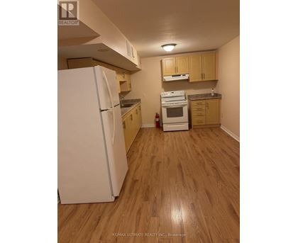 A white refrigerator stands in a kitchen with wooden floors and cabinets.