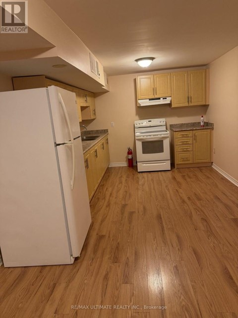 A white refrigerator stands in a kitchen with wooden floors and cabinets.