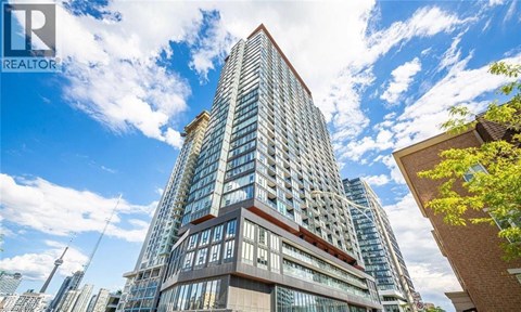 A tall building with a glass facade stands in front of a partly cloudy sky.