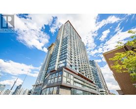 A tall building with a glass facade stands in front of a blue sky with clouds.