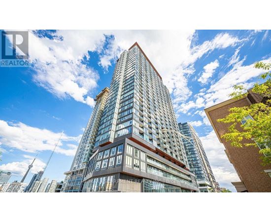 A tall building with a glass facade stands in front of a blue sky with clouds.