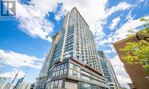 A tall building with a glass facade stands in front of a blue sky with clouds.