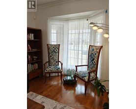 Two chairs with blue and white patterned cushions are in front of a window with white curtains.