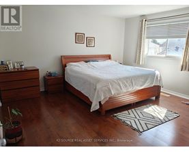 A bedroom with a bed, nightstand, and a plant.