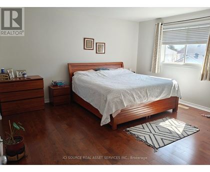A bedroom with a bed, nightstand, and a plant.