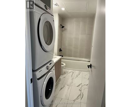 A white tiled bathroom with a washer and dryer stacked on top of each other.