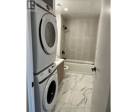 A white tiled bathroom with a washer and dryer stacked on top of each other.