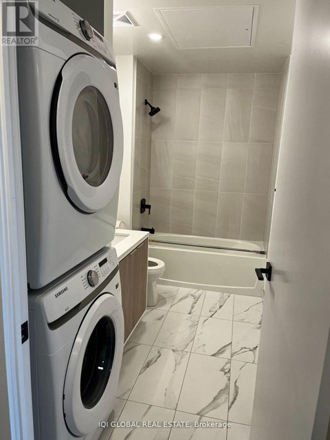 A white tiled bathroom with a washer and dryer stacked on top of each other.