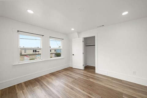 A room with wooden floors and white walls, with a window showing a view of a building and a door on the right.