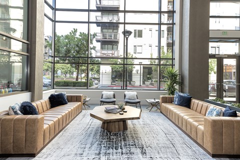 A large room with tan couches and a coffee table in front of large windows.