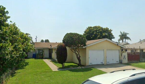 A house with a white garage door is surrounded by greenery.