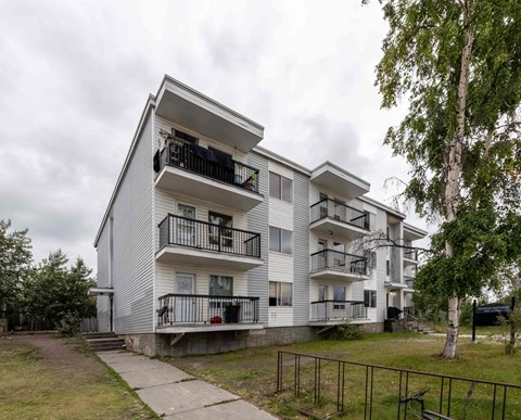 A modern apartment building with balconies and a small garden area.