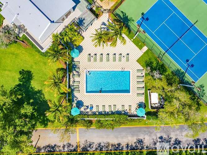 An aerial view of a pool surrounded by palm trees and a tennis court.