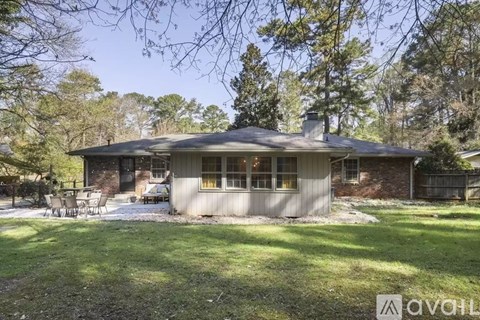A house with a grey roof and a white fence is surrounded by trees.