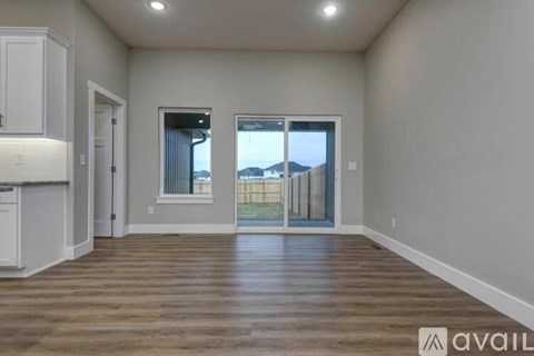 A spacious room with wooden flooring and a view of a fence and trees outside the window.