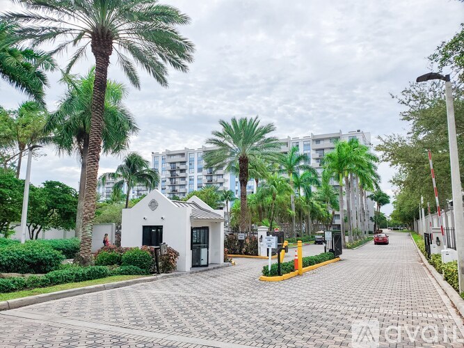 A white building with a black door is surrounded by palm trees and a brick road.