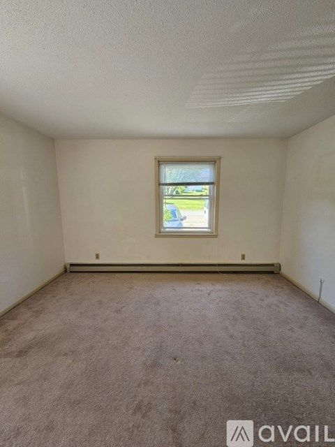 A room with a carpeted floor and a window showing a parking lot outside.