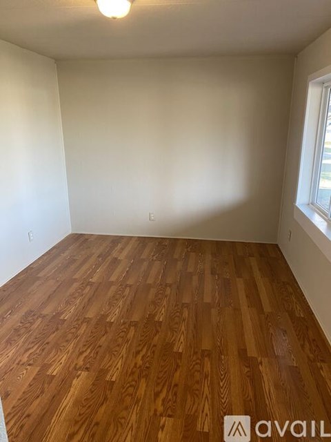 A room with wooden flooring and a window on the right side.