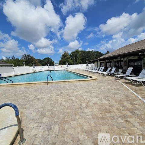A pool surrounded by a brick patio and lounge chairs.