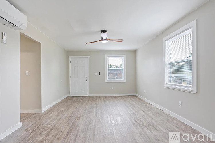 A spacious room with a ceiling fan and light, hardwood floors, and a window with blinds.