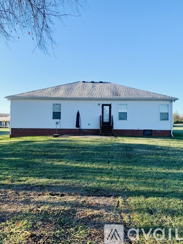 A white house with a black door and windows is surrounded by a grassy area.