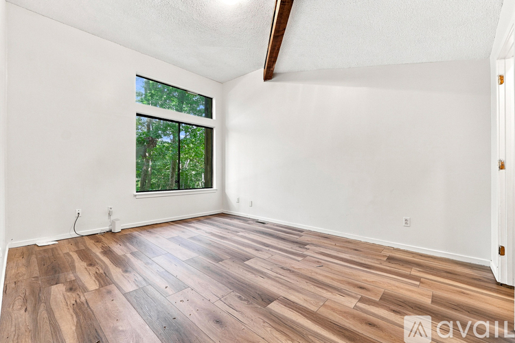A room with wooden flooring and a window showing trees outside.