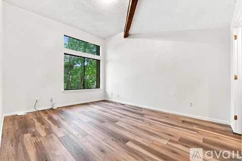 A room with wooden flooring and a window showing trees outside.