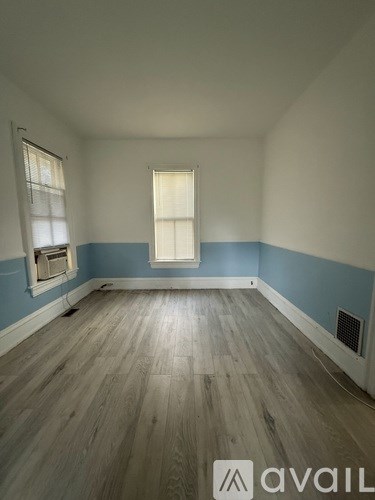 A room with wooden flooring and a window with white curtains.