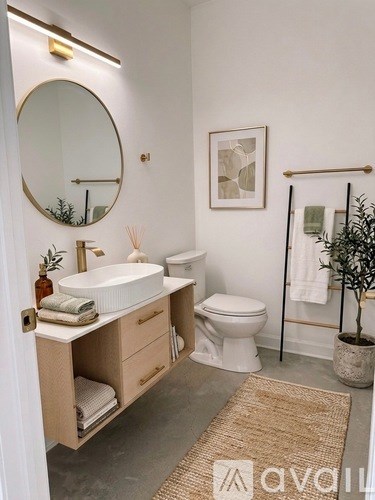A bathroom with a round mirror, a white sink, a toilet, and a potted plant.