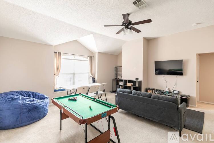 A pool table with a green cloth is in the middle of a room with a bean bag chair and a television.