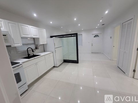 A kitchen with white cabinets and appliances, a glass door refrigerator, and a white tiled floor.