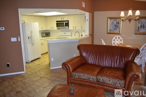 A brown leather couch sits in a kitchen with a refrigerator and microwave.