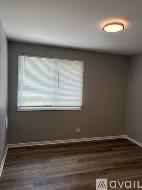 A room with a window covered by white blinds and wooden flooring.