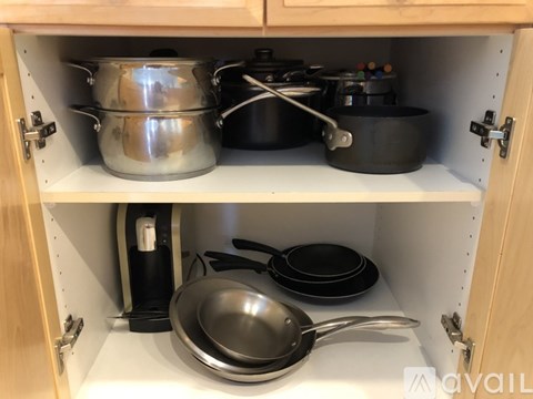 A kitchen cabinet with pots, pans and a frying pan.
