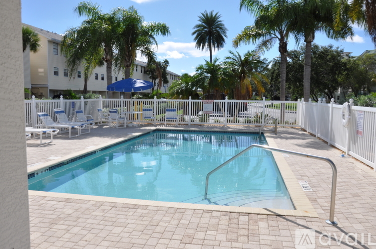 A pool surrounded by chairs and a fence with a view of a body of water and a house in the background.