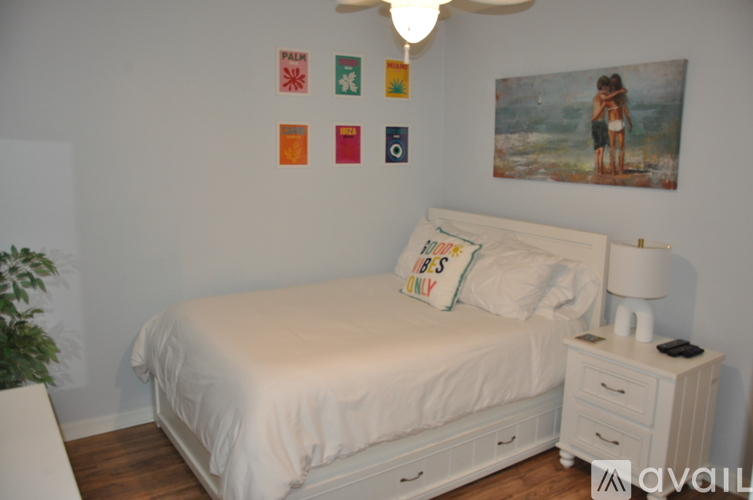 A bedroom with a white bed and a painting on the wall.