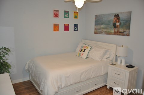 A bedroom with a white bed and a painting on the wall.