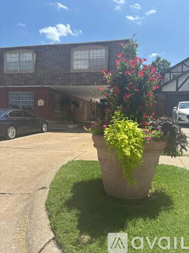 A large planter with red and green flowers sits on a green lawn in front of a house.