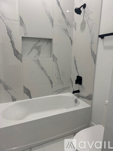 A bathroom with a marble patterned wall and a white bathtub.