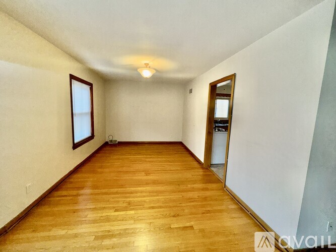 A room with wooden floors and white walls, with a window on the left wall.
