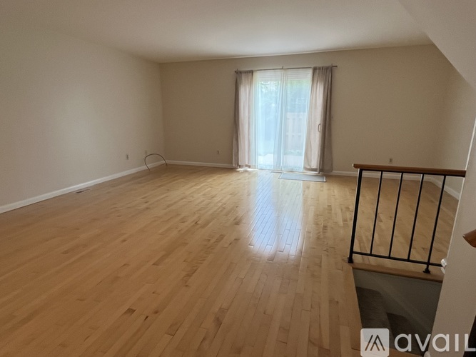 A spacious room with wooden flooring and a window with curtains.