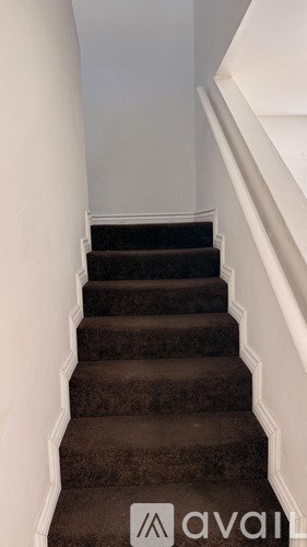 A staircase with a brown carpeted runner and white walls.