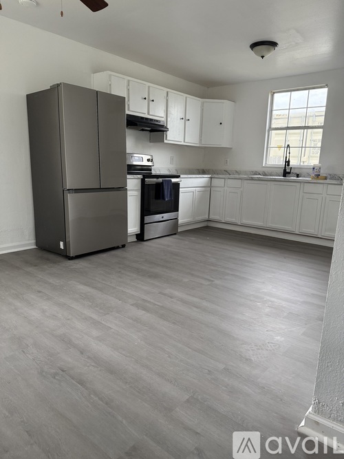 A kitchen with a grey refrigerator, white cabinets, and a window.