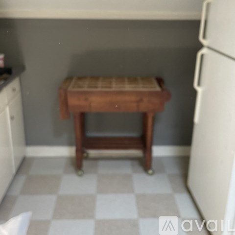 A white fridge sits next to a wooden stool in a kitchen.