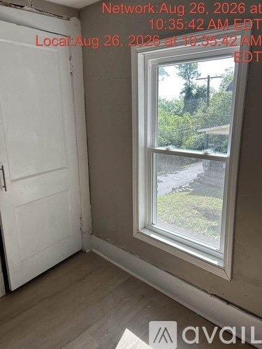 A room with a white door and a window showing a view of a green area outside.