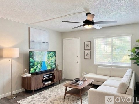 A living room with a television, a couch, a coffee table, and a ceiling fan.