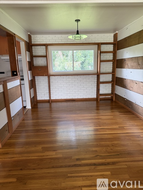 A room with wooden floors and a window with a view of trees.