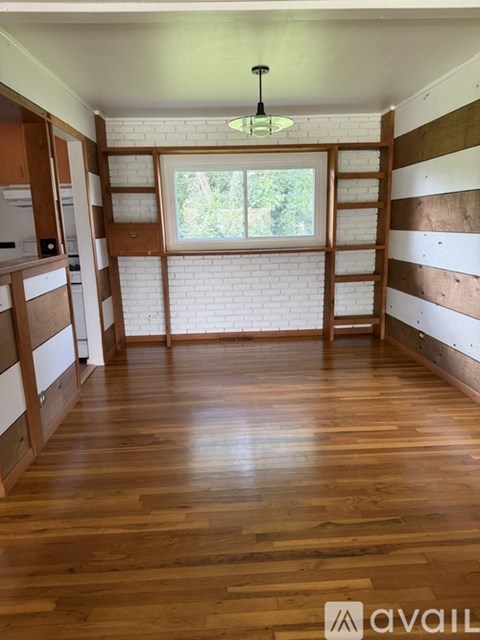A room with wooden floors and a window with a view of trees.